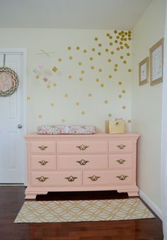 a pink dresser with gold polka dots on the wall in a baby's room