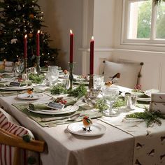 a table set for christmas dinner with candles and place settings on the dining room table