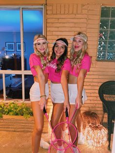 three girls in pink shirts and white shorts holding tennis racquets while standing next to each other