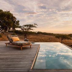 a lounge chair sitting on top of a wooden deck next to a swimming pool at sunset