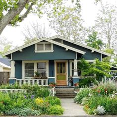 a blue house with flowers and trees in the front yard