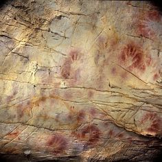 an artistic rock wall with red and white paint on it's surface, including hand prints