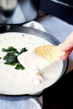 a hand dipping a cracker into a bowl of white dip with cilantro and parsley