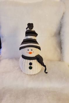 a snowman sitting on top of a chair covered in white fluffy blankets and a black hat