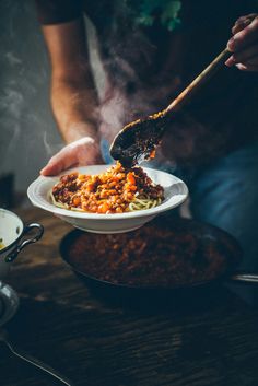 a person is holding a bowl of food with noodles and meat on the side while stirring it