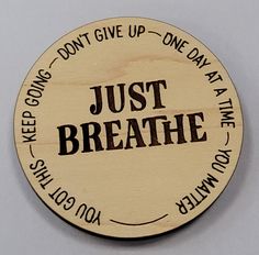 a wooden badge with the words just breathe written in black and white ink on it