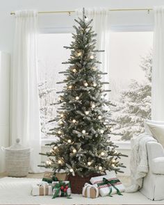 a decorated christmas tree in front of a window with presents under it and lights on