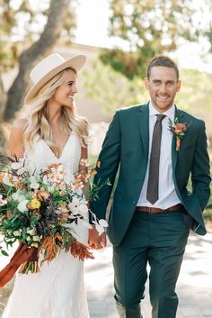 a bride and groom walking down the street holding hands with flowers in their bouquets