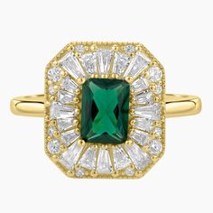 an emerald and white diamond ring in yellow gold with diamonds around the band, set against a white background