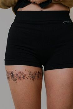 a woman wearing black shorts with flowers on the side and tattoos on her lower back