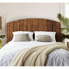 a bed with white sheets and pillows in a bedroom next to a potted plant