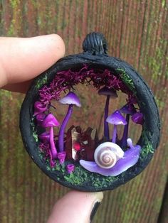 someone is holding a miniature garden with purple mushrooms and other things in the bowl,