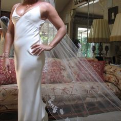 a woman wearing a wedding dress and veil standing in front of a couch with her hands on her hips