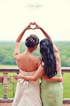 two women standing next to each other with their arms in the shape of a heart