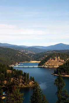 a large body of water surrounded by trees and mountains on a sunny day with blue sky