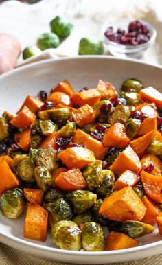 a white bowl filled with brussel sprouts and sweet potatoes next to cranberry sauce