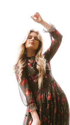 a woman in a floral dress posing for the camera with her hand up to her head