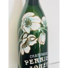 a green bottle with white flowers painted on the top and bottom, in front of a white wall