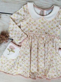 Swoon Baby Autumn Wildflower Embroidery Pocket Dress Style 23-26. Ready to ship! Description: This beautiful dress is made of high quality knit fabric. Swoon Baby knits are extremely soft and comfortable. Sizing: Swoon Baby fits true to size. We offer matching bows & knee high socks in our main menu. Link: https://southernsweetchildren.com/collections/accessories?page=1 If you have any questions or need a measurement, please contact our shop at amanda@southernsweetchildren.com Cute Floral Applique Dresses For Garden Party, Cute White Dress With Embroidered Hem, Cream Cotton Dress For Garden Party, Pink Embroidered Long Sleeve Dress, Cute Long Sleeve Cotton Dress, Long Sleeve Cotton Dress With Floral Applique, Cute White Dress With Floral Embroidery, Pink Long Sleeve Dress With Floral Applique, Playful Long Sleeve Cotton Dresses