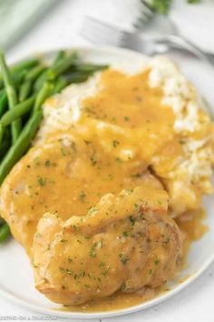 a white plate topped with meat covered in gravy next to green beans and mashed potatoes