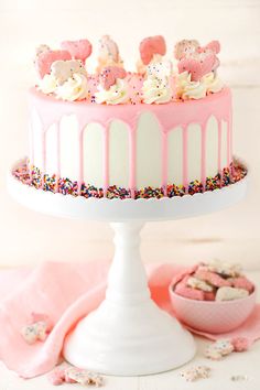 a white cake with pink frosting and sprinkles on top sitting on a table