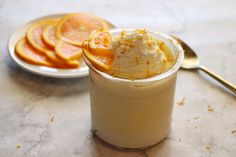 an orange dessert in a small glass with whipped cream and sliced oranges on the side