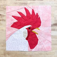 a red and white rooster quilted on top of a wooden table next to a piece of paper