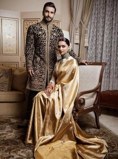 a man and woman standing next to each other in front of a couch with gold cloths on it