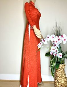 a mannequin dressed in an orange dress next to a vase with white flowers