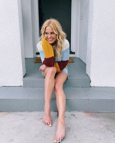 a woman sitting on the steps in front of a white building with her legs crossed