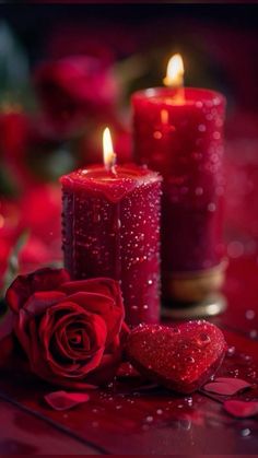 two red candles with hearts and roses on the table next to them, one is lit