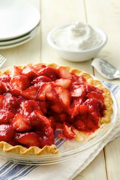 a pie with strawberries in it sitting on a table next to plates and utensils