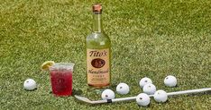 a bottle of alcohol sitting on top of a green field next to golf balls and a tee