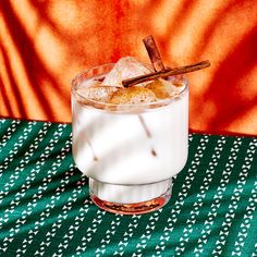 a glass filled with ice and cinnamon on top of a green table cloth next to an orange wall