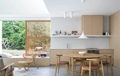 an open kitchen and dining room area with wooden furniture in the foreground, large windows to the outside