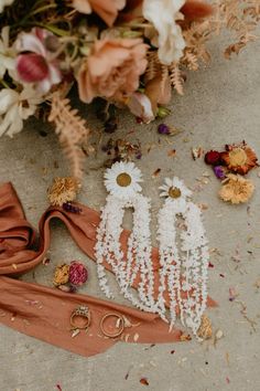 two pairs of earrings laying on the ground next to flowers and other things that are scattered around them