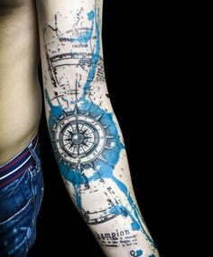 a man's arm with a compass tattoo on it and blue ink splatters