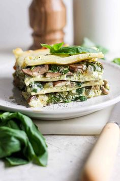 a stack of food sitting on top of a white plate next to spinach leaves