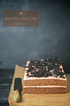 a piece of chocolate layer cake sitting on top of a wooden cutting board