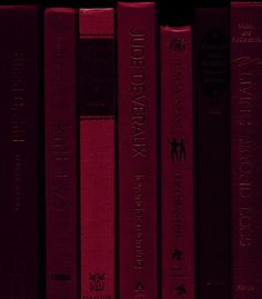 a row of red books sitting next to each other on top of a book shelf