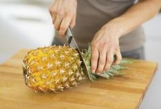 a person cutting up a pineapple on top of a wooden cutting board with a knife