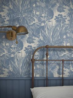 a bed in a bedroom with blue wallpaper and a metal headboard, next to a lamp