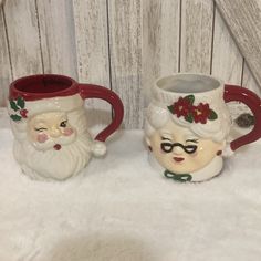 two ceramic mugs decorated with santa claus and snowmen on white fur covered surface