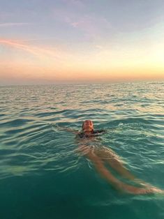 a woman swimming in the ocean with her head above the water's surface as the sun sets