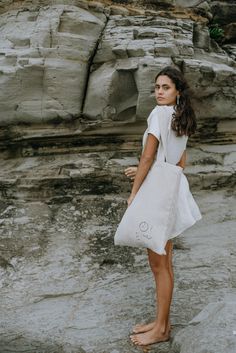 a woman standing on top of a rock covered beach next to a large white bag