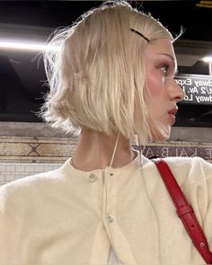 a woman with blonde hair wearing headphones and a white sweater is standing in a subway station