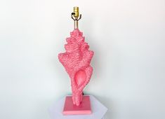 a pink sculpture with a gold lamp on it's end sitting on top of a white table