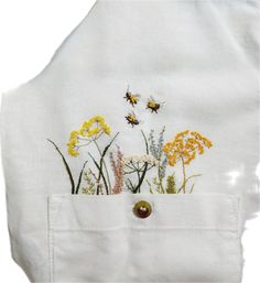 a white shirt with flowers and bees embroidered on the chest pocket, in front of a white background