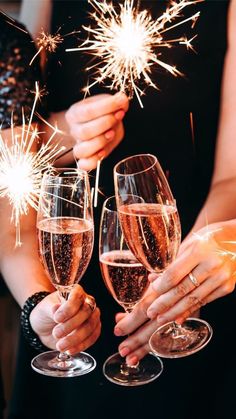 three people holding wine glasses with sparklers in the background and two champagne flutes in their hands