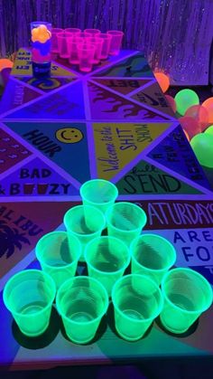 glow in the dark cups are sitting on a table with purple and green lights around them